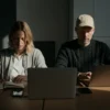 Two people working together, focused, each wearing AirPods, in a collaborative workspace.