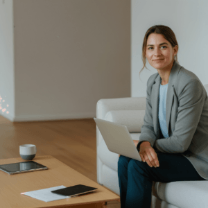 Woman sitting on a couch with a laptop on her lap, smiling at the camera.