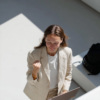 A woman sits in front of her laptop, celebrating with a fist pump and a joyful expression.